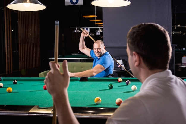 Adult men with disabilities in a wheelchair play billiards in the club