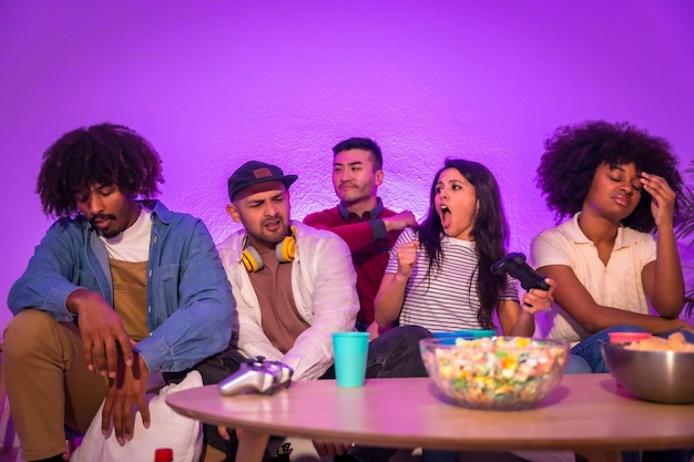 성인 파티 소파에 앉아 팝콘 조이스틱이나 컨트롤러를 손에 들고 비디오 게임을 하는 젊은 사람들이 레이스 승리를 축하하는 보라색 LED 여성