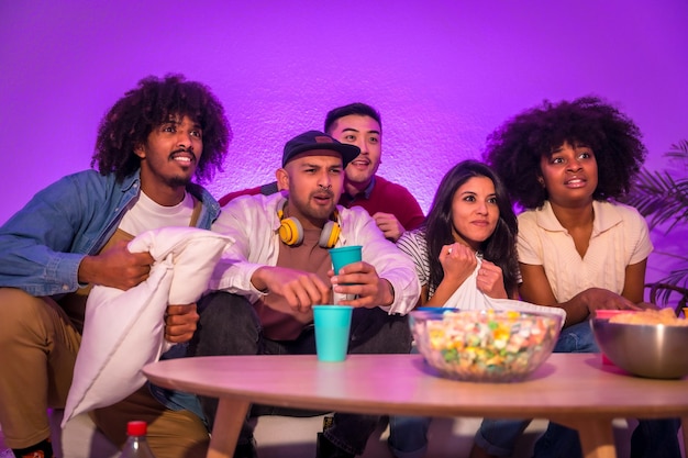 Adult party young people sitting on the sofa watching a football game with popcorn excitement for soccer purple led nervous about the game