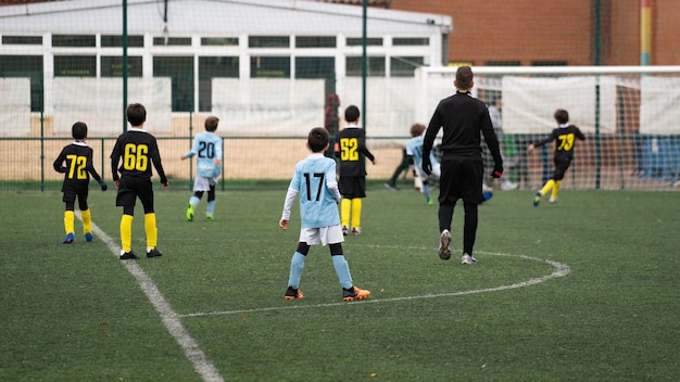 Adult referee dressed in black watching kids soccer move towards goal with attention during a match