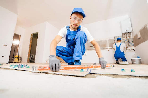 Adult repairman in a special uniform laying tiles on the floor in a new house