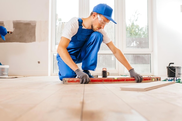 Adult repairman in a special uniform laying tiles with tile leveling system on the floor in a new ho