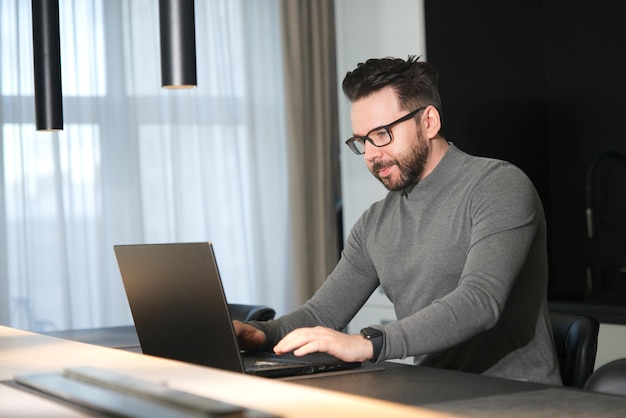 Adult serious man freelancer is working on laptop computer in glasses at home Freelance