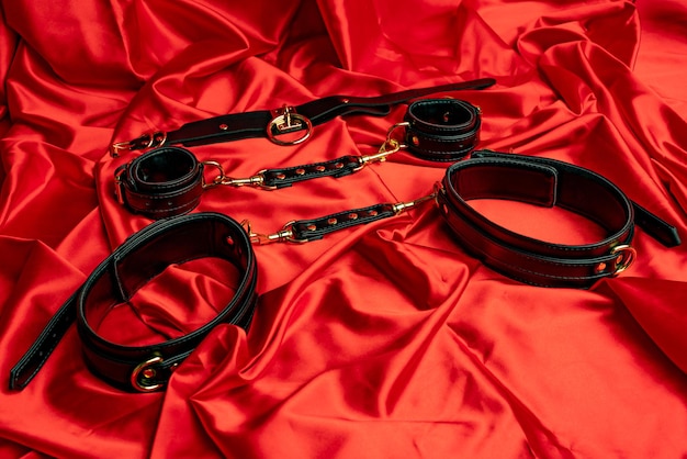 アダルトセックスゲーム。 BDSMアイテム。レザーストラップの手錠、赤いサテンのシーツの襟。