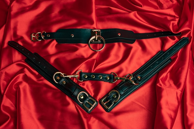 Photo adult sex games bdsm items leather straps handcuffs and gag ball on a red satin sheet