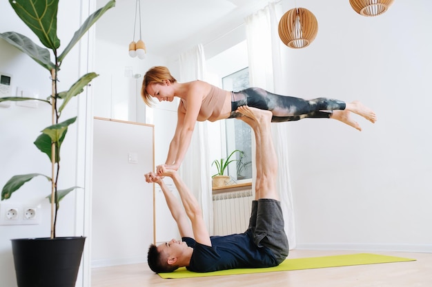 Adult siblings doing yoga at home Brother lifting sister with his legs