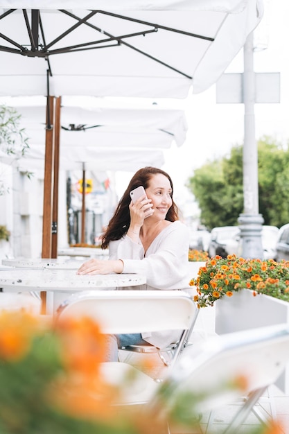 Adult smiling brunette woman forty years using mobile phone in cafe at city street