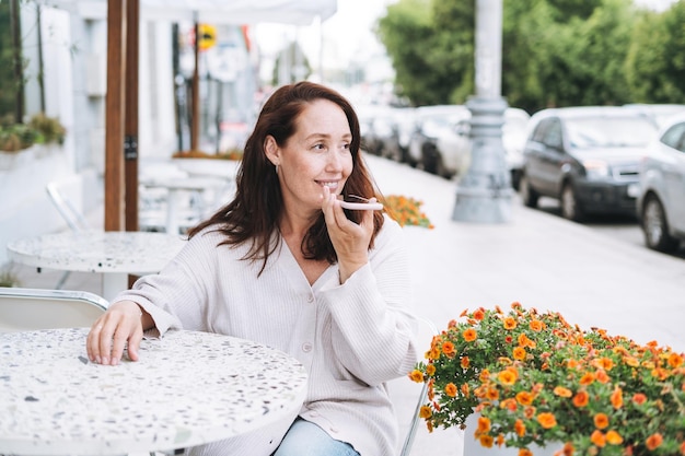 Adult smiling brunette woman forty years using mobile phone in cafe at city street