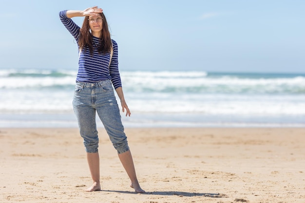 An adult smiling woman stand on sea beach and covering her face from the sunlight