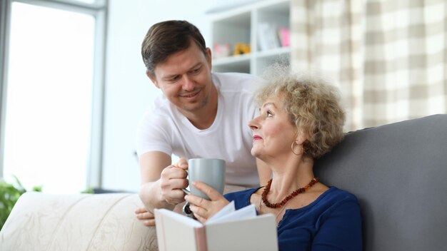 成人した息子が年配の母親にお茶を差し出している