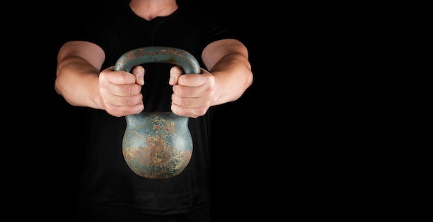 Foto atleta adulto forte in abiti neri che tiene un kettlebell di ferro sulle braccia stese nere