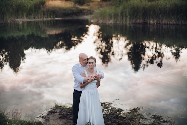 Adult strong man without hair in white shirt and black trousers with a woman with blonde hair in long white dress