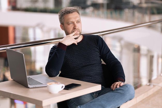 Adult successful man sitting in a cafe with laptop and smartphone and thinking about future project