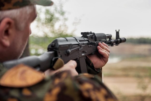 Adult war team games with weapons, airsoft or strikeball, in forest. Army soldier in military camouflage uniform with glasses, weapon in hands. Middle-aged soldier in woodland uniform with autogun