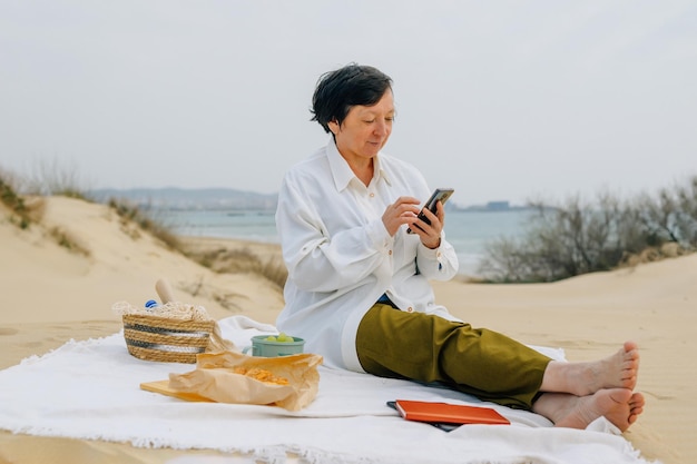 Foto donna adulta sulla spiaggia in primavera estate ordina prodotti online per un picnic acquista spedizione veloce