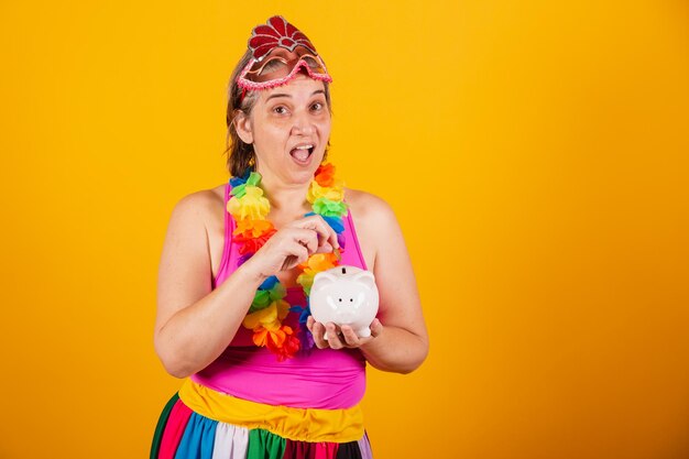 Adult woman in carnival clothes smiling at camera holding piggy bank and coin