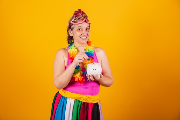 Adult woman in carnival clothes smiling at camera holding piggy bank and coin