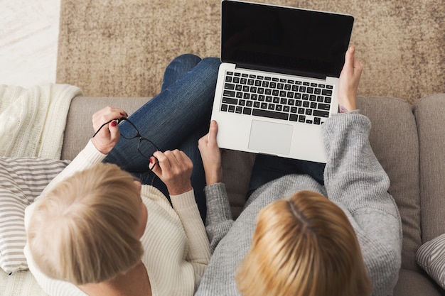 Adult woman and daughter using laptop with blank screen for advertisement, copy space. Generation, relationship, modern technology concept, top view