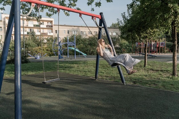 adult woman in dress rides on a children swing at the playground
