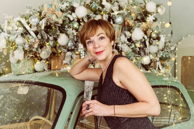 写真 大人の女性が大晦日にクリスマス ツリーの横にあるヴィンテージ車でシャンパンを飲む