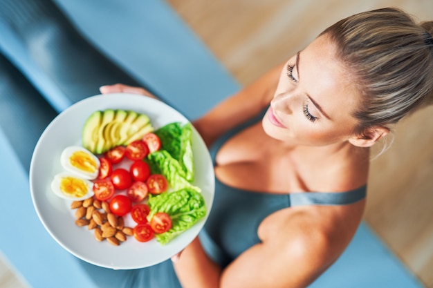 adult woman eating healthy lunch and sitting on yoga mat