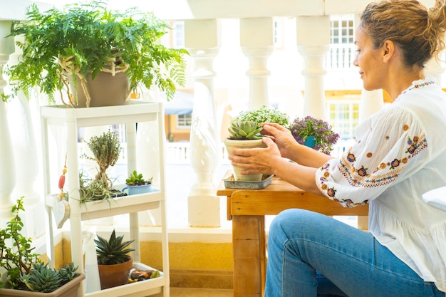 Adult woman in gardening activity outside home in the terrace Female people caring plants for environment and green lifestyle concept Happy lady regrowth plants outside