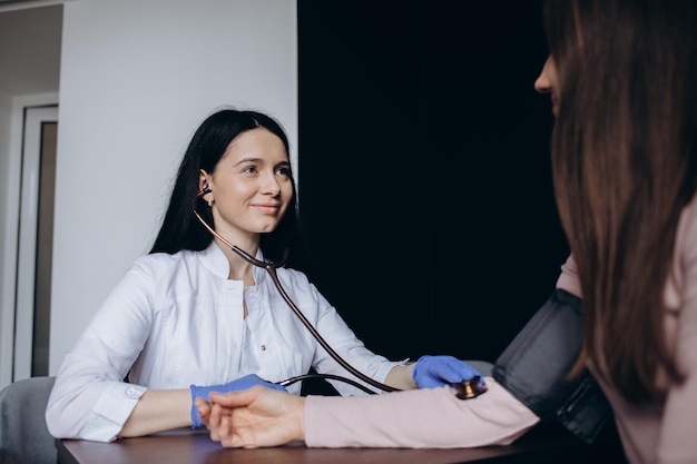 Adult woman having blood pressure test during visit at female doctor's office