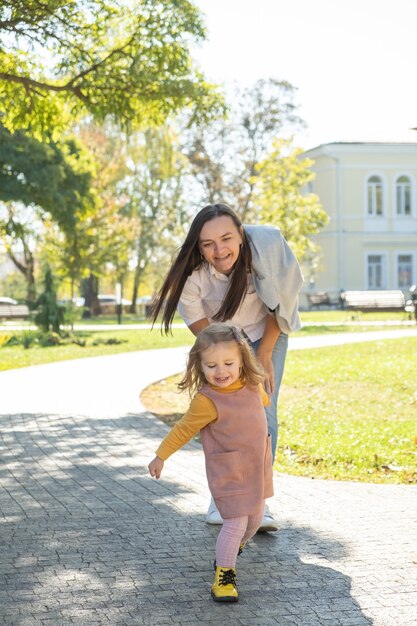 Adult woman having fun, catch-up her child daughter in green park.