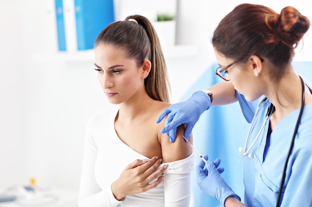 Adult woman having injection during visit at female doctor's office