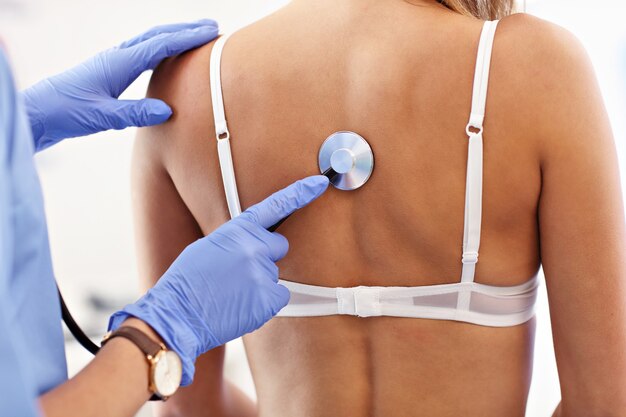 adult woman having a visit at female doctor's office and being examined with stethoscope