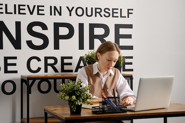 An adult woman is working hard at a laptop and making notes in agenda