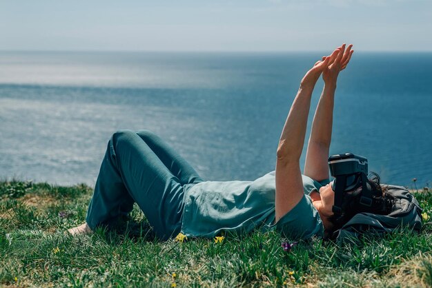 Foto donna adulta giace in montagna sullo sfondo del mare in estate primavera in occhiali di realtà virtuale
