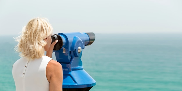 Adult woman looking through binocular viewer on the sea landscape