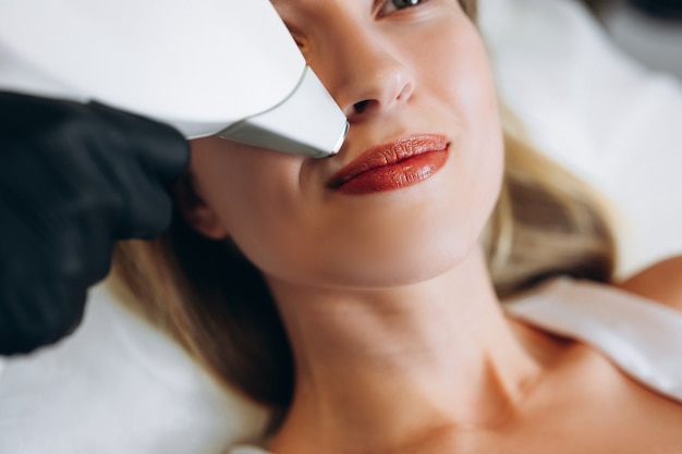 Foto donna adulta sdraiata sul tavolo medico nella clinica di bellezza, con depilazione laser nel salone di bellezza professionale. estetista femminile in uniforme utilizzando la macchina per la depilazione laser.