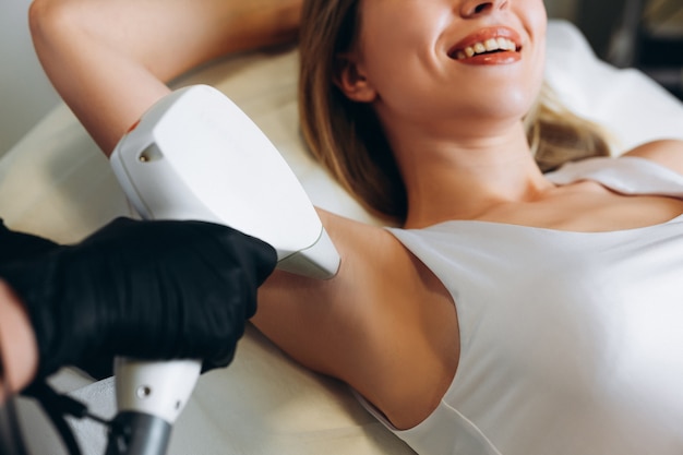 Фото Взрослая женщина, лежа на медицинском столе в клинике красоты, имея лазерную эпиляцию в профессиональном салоне красоты. женский косметолог в униформе с помощью машины для лазерной эпиляции.