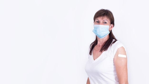 Photo adult woman in mask with bandaid on shoulder after vaccination against coronavirus or flu mandatory