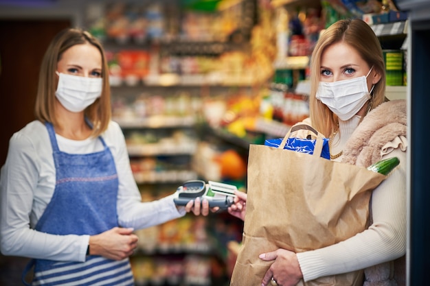 Donna adulta in maschera medica che preleva l'ordine online dal negozio di alimentari