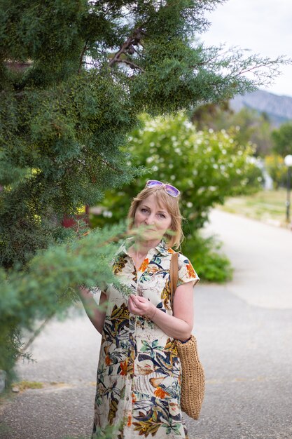 An adult woman near a green tall thuja in a city park.