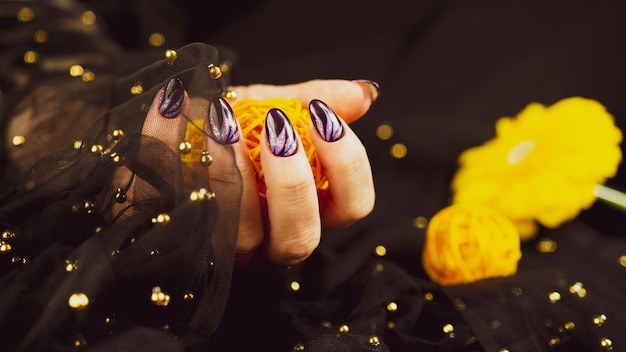 Adult woman's hand with purple manicure on black background Crop unrecognizable person with design on nails Concept of care and beauty