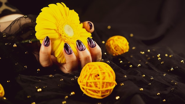 Adult woman's hand with purple manicure on black background Crop unrecognizable person with design on nails holding yellow flower