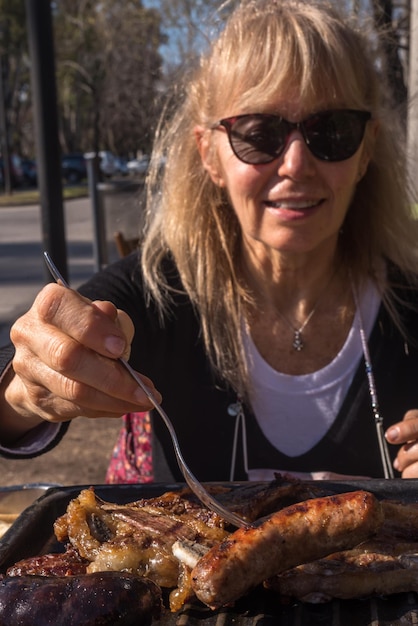 Photo adult woman skewering a pork chorizo with fork from an argentinean barbecue