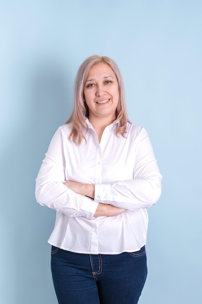 An adult woman smiles with her arms crossed standing on a blue background