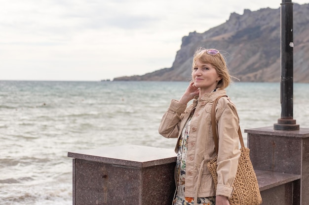 Adult woman smiling on the sea embankment Vacation on the sea coast in autumn