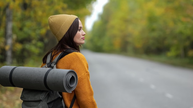 大人の女性が道路の近くに立ち、森でバスを待つ