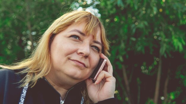 Взрослая женщина разговаривает по смартфону крупным планом Женщина разговаривает по мобильному телефону и смотрит в сторону Красивая женщина разговаривает по телефону во время прогулки
