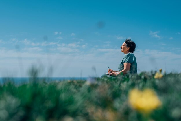 写真 大人の女性が海を背景に山の晴れた日に計画日記を思慮深く書く