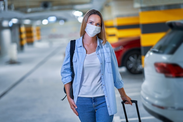 adult woman tourist wearing mask due to covid-19 procedures in underground airport parking lot