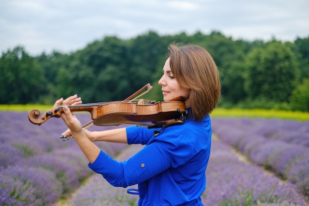 Foto violinistessa adulta che suona il violino in un campo di lavanda estivo