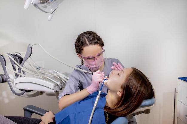 Взрослая женщина, посещающая стоматологический кабинет. Руки дантиста в резиновых защитных перчатках с использованием белого полировального камня для пациента.