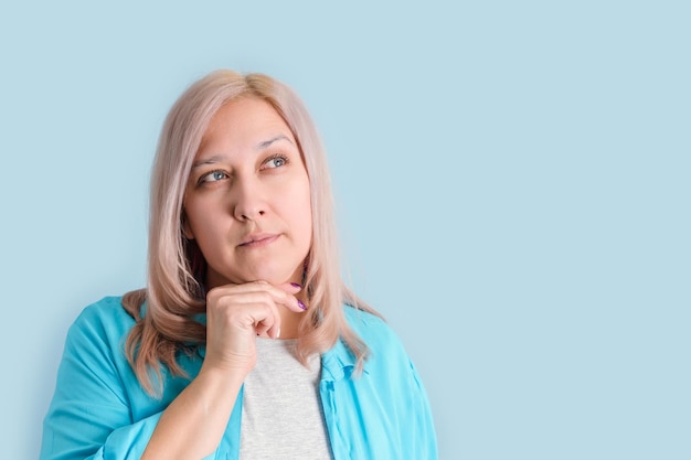 An adult woman was thinking with her hand under her chin standing on a blue background copyspace